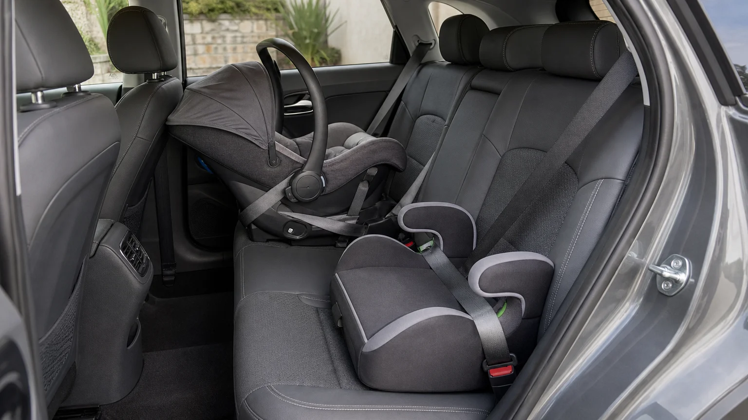 Rear-facing infant seat and booster seat arranged inside a grey 2021 electric Kia e-Niro.