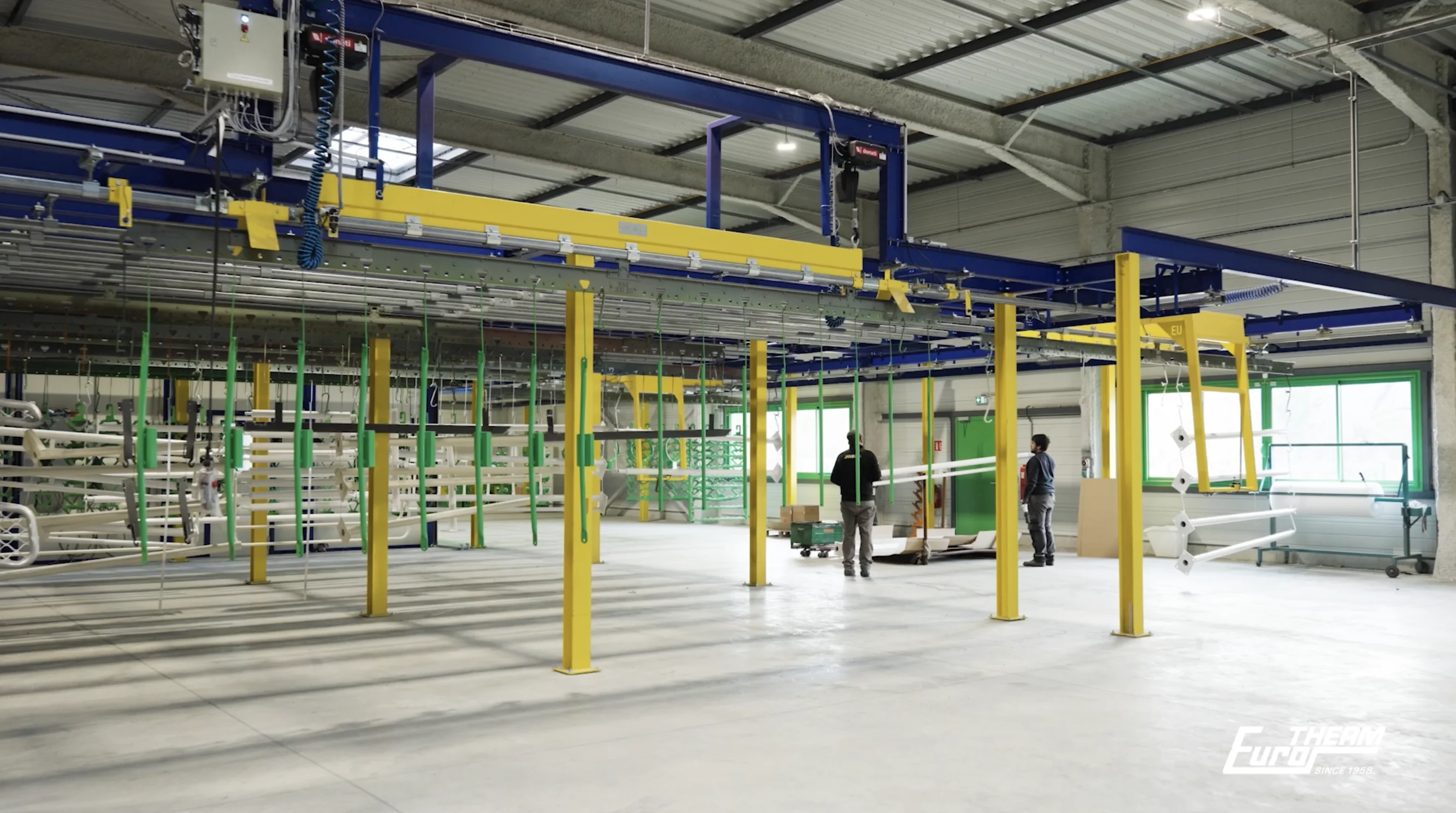 Intérieur d’une installation industrielle avec équipements suspendus, structures métalliques et postes de travail
