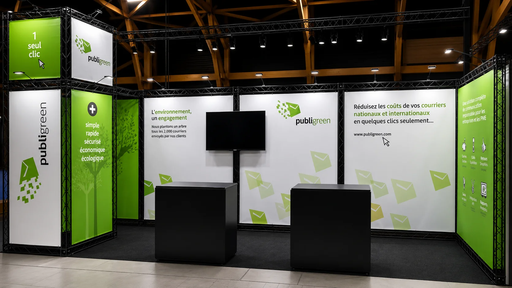 Stand d’exposition avec panneaux imprimés verts et blancs, comptoirs et écran sous une structure d’éclairage