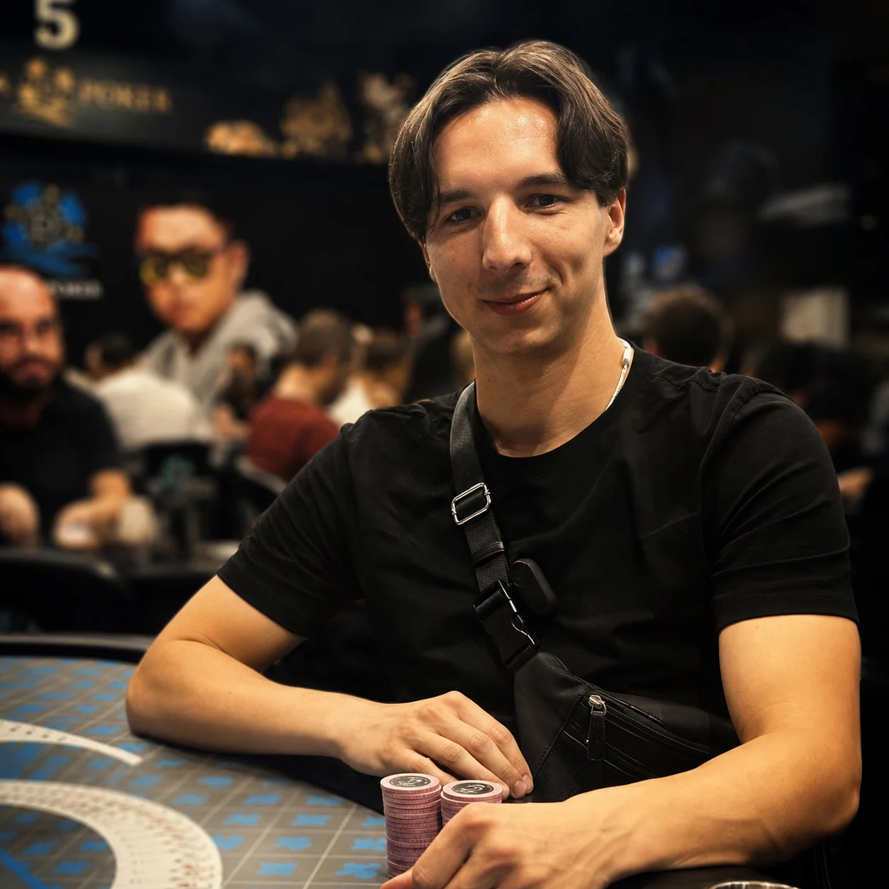 Une personne assise à une table de poker tient des jetons roses, dans une salle de jeu intérieure floue.