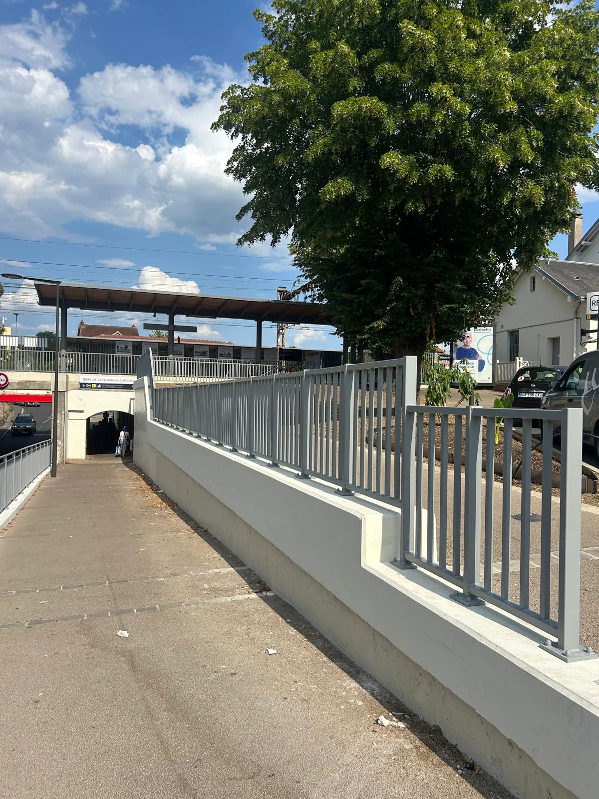 Allée piétonne pavée longeant une rambarde métallique et un muret bas près d’un bâtiment