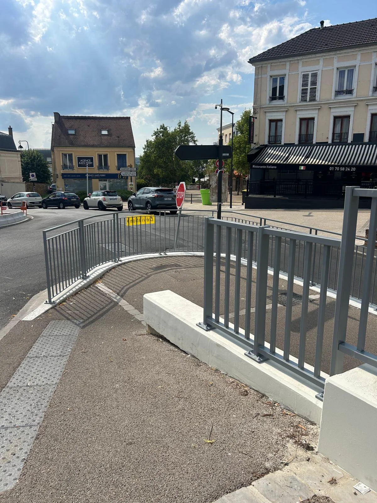 Intersection urbaine avec garde-corps métalliques, chaussée, véhicules et bâtiments bas