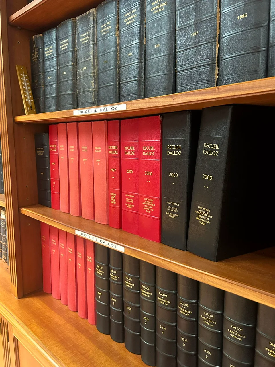 Rangées de volumes de référence juridiques reliés sur une étagère en bois, avec la mention Recueil Dalloz