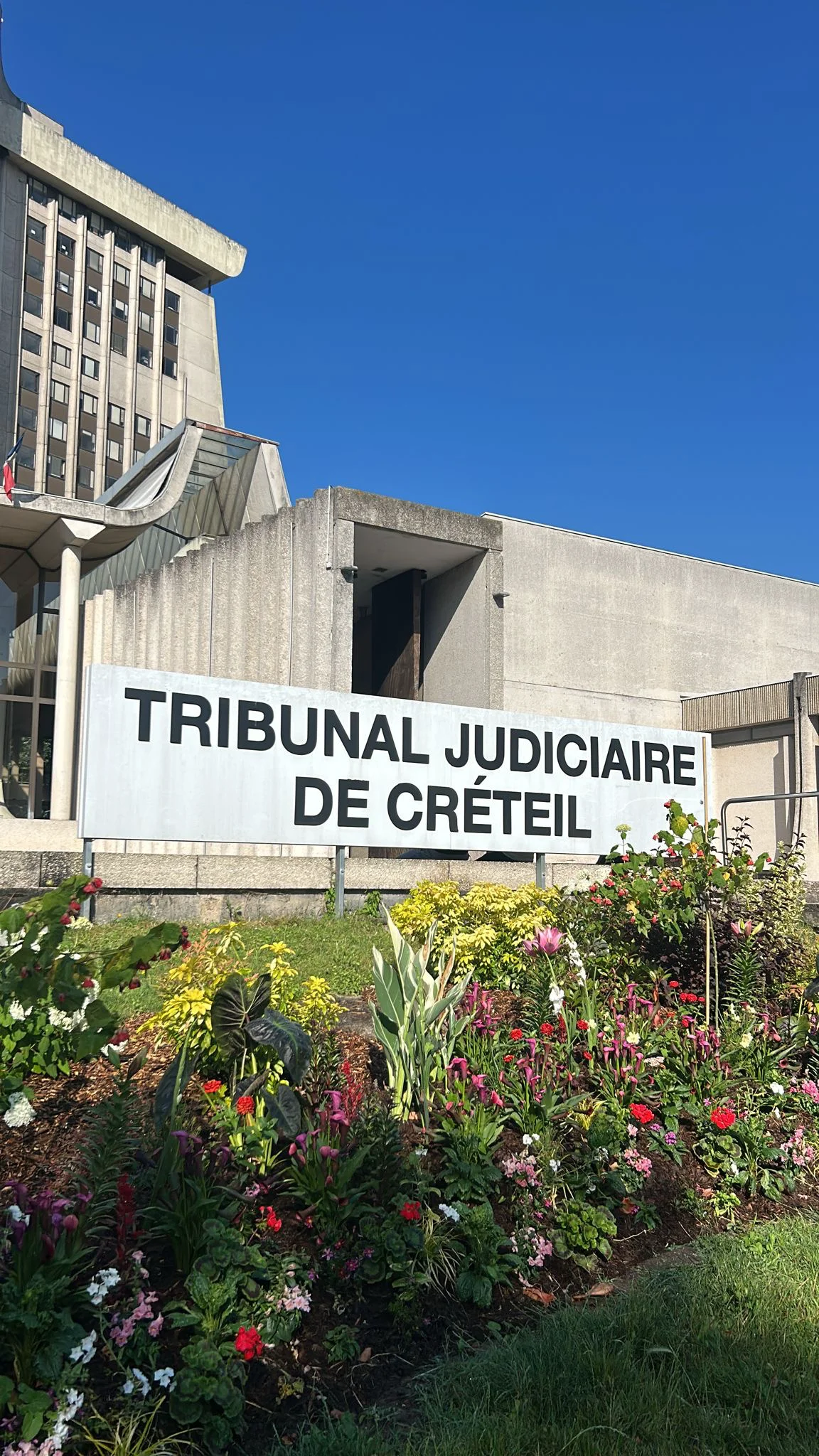 Façade en béton du Tribunal Judiciaire de Créteil avec sa signalétique et un parterre fleuri au premier plan