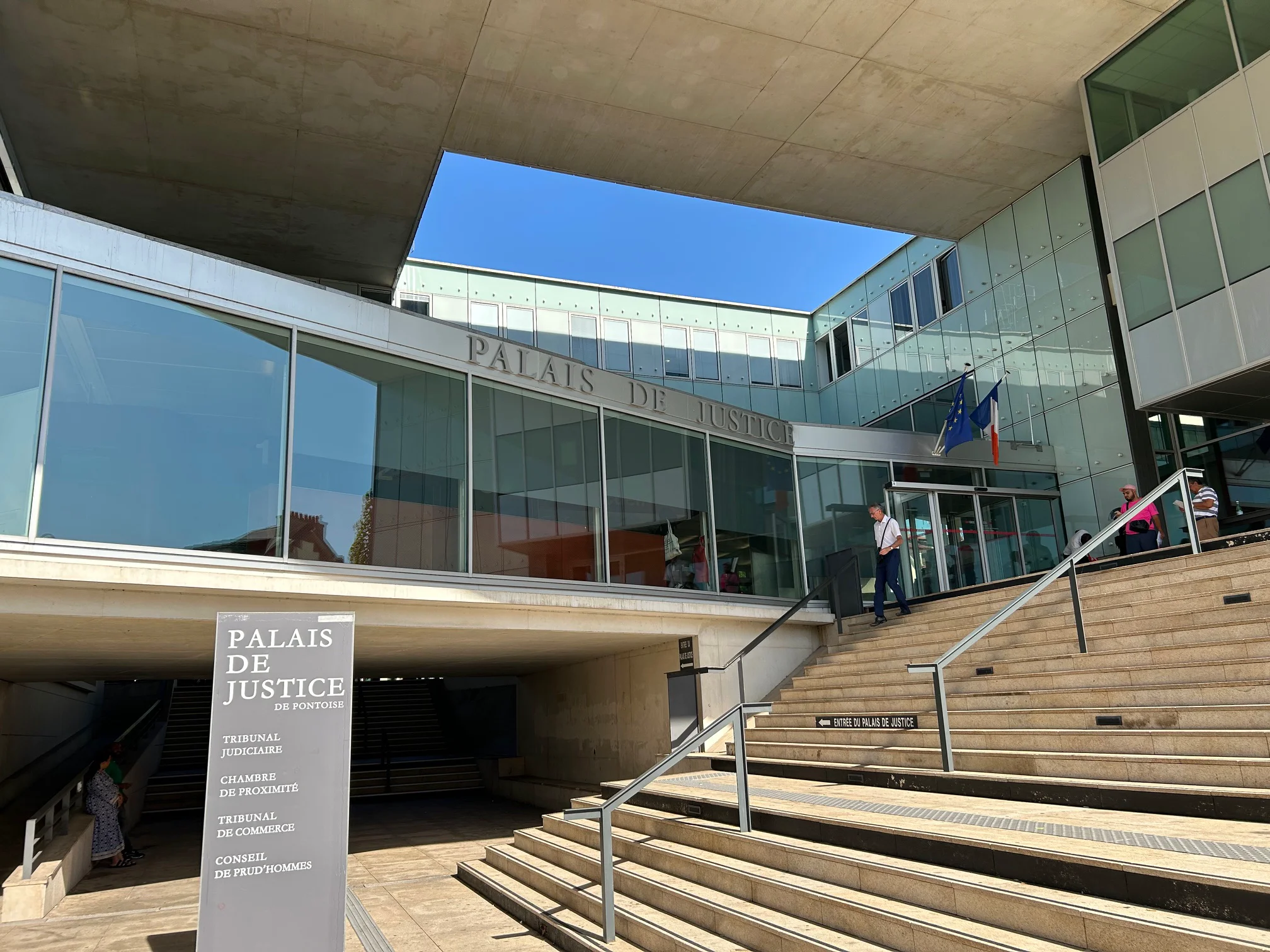 Entrée vitrée moderne d’un Palais de Justice avec escaliers et drapeaux