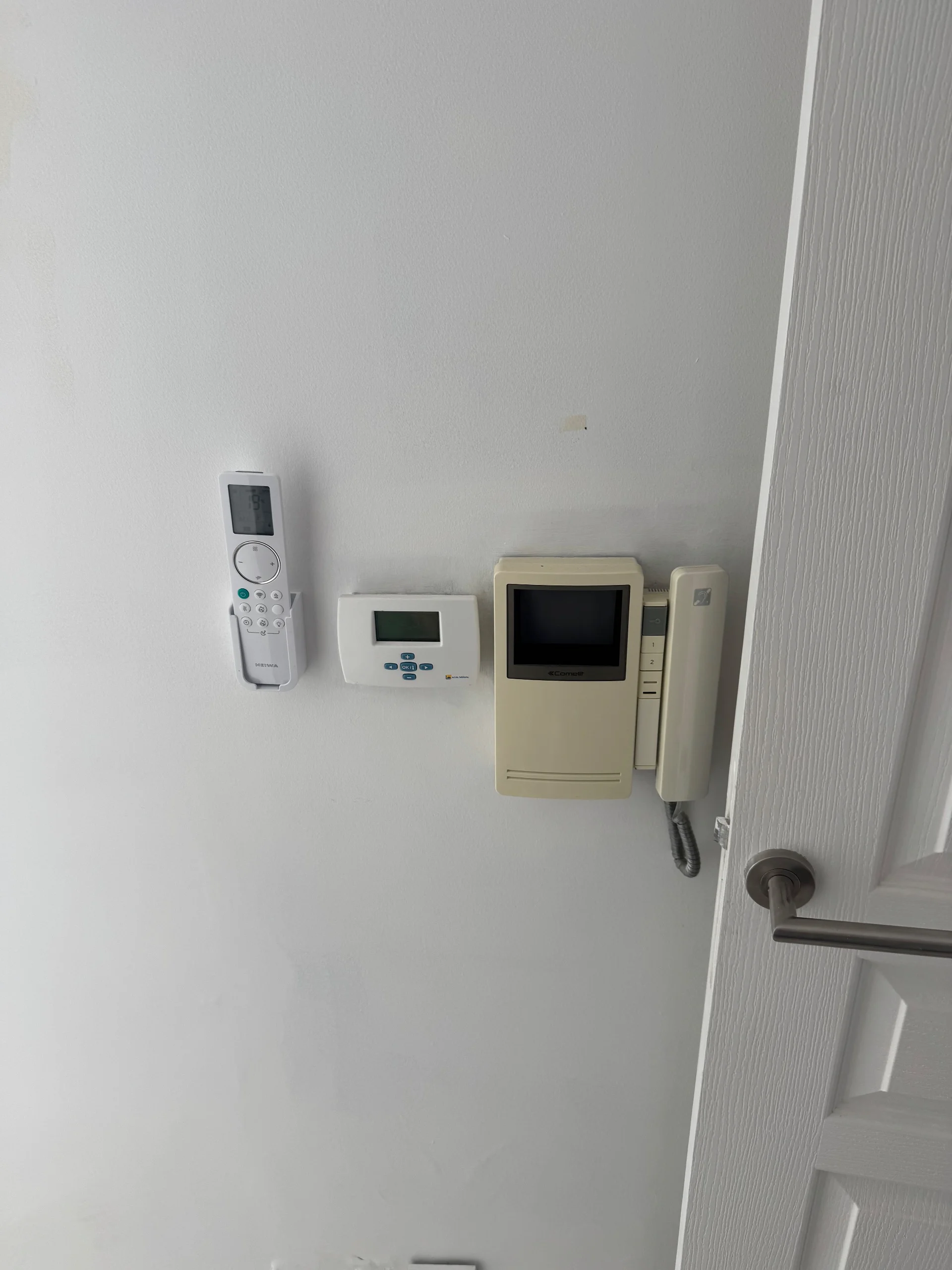 Télécommande murale dans son support, panneau de commande et interphone à côté d’une porte.